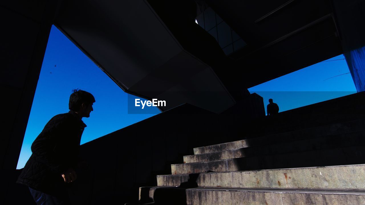 LOW ANGLE VIEW OF SILHOUETTE MAN STANDING BY STAIRCASE AGAINST SKY