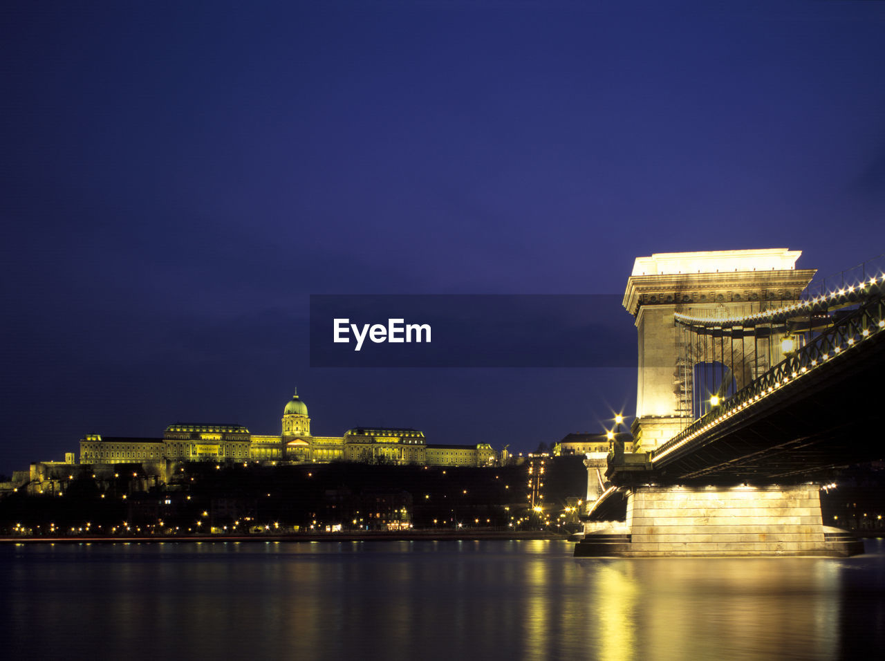 Illuminated chain bridge over river danube by buda castle against sky at dusk