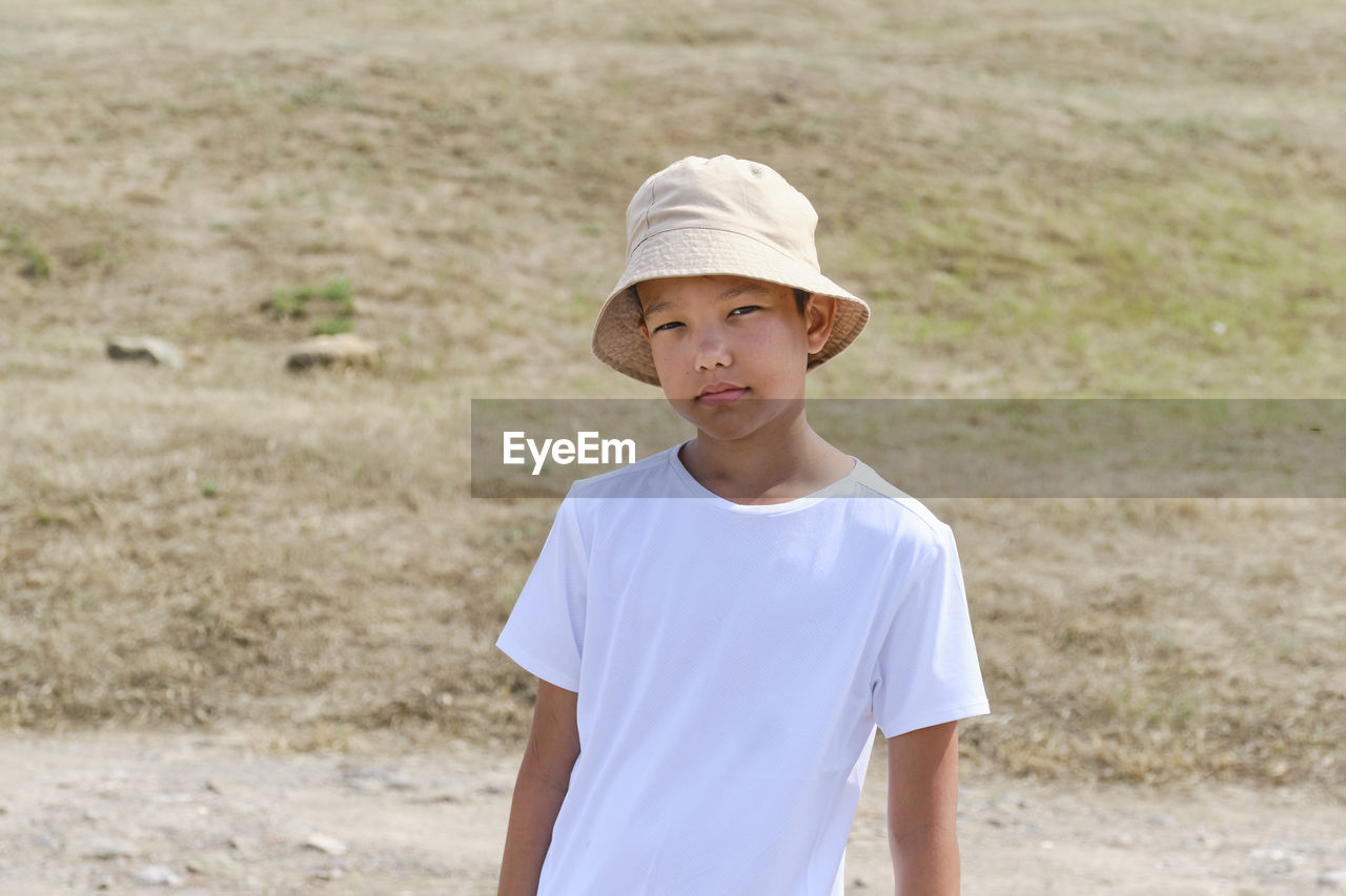 Half-length portrait of an asian boy in white t-shirt and panama hat, against background of nature.