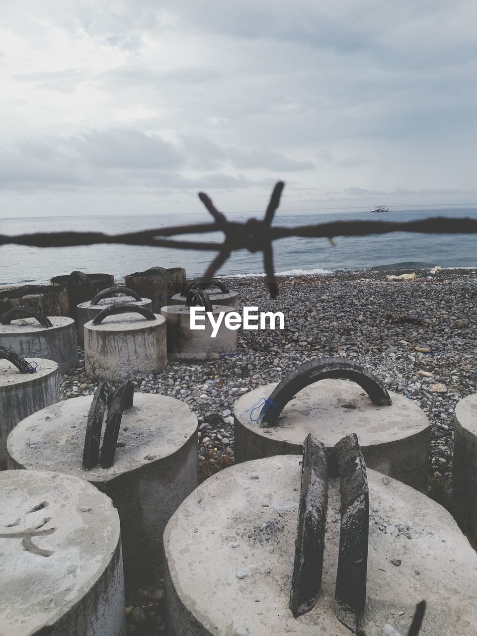 Barbed wire over rocks at beach against sky