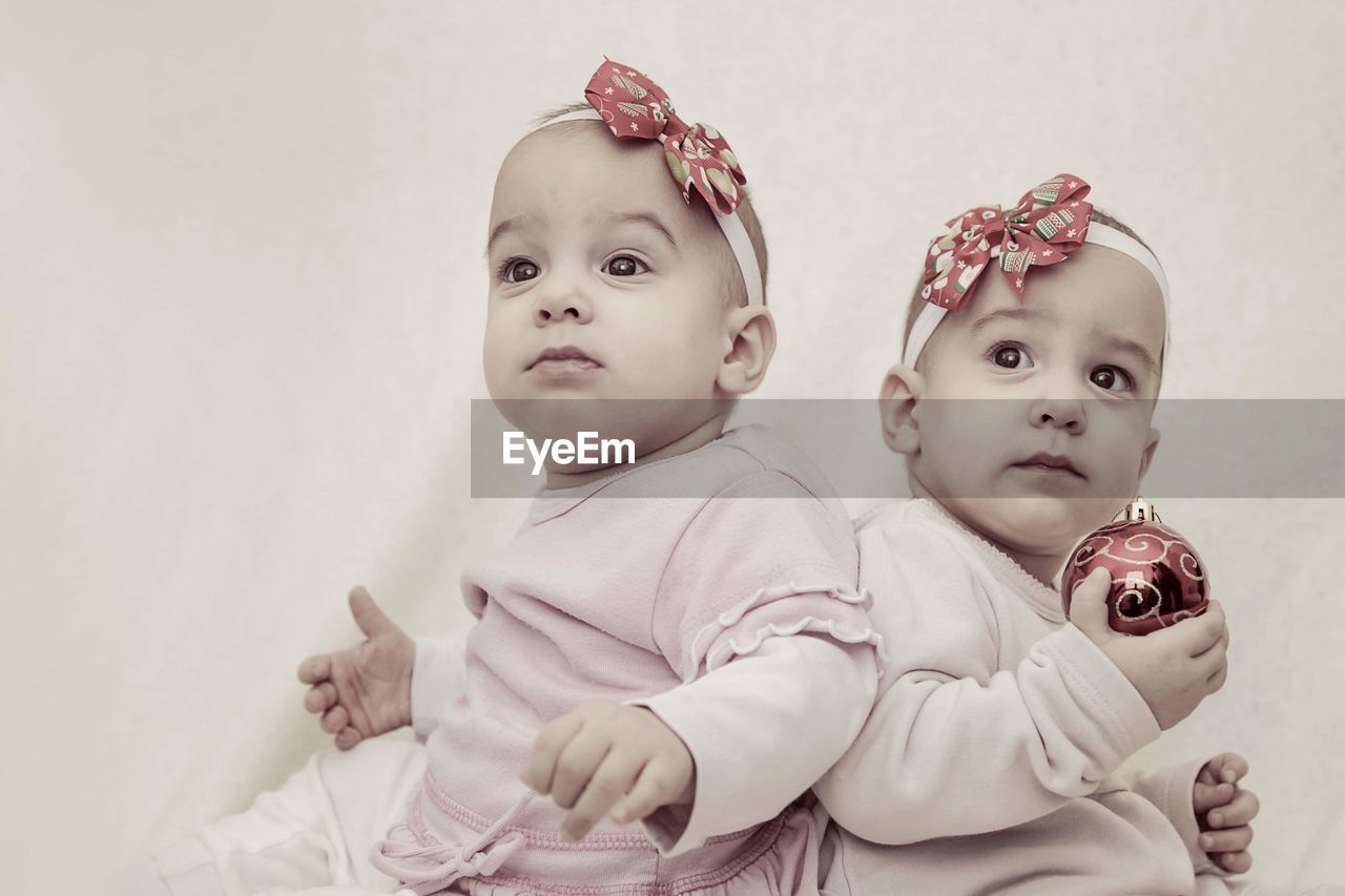 Cute twin baby girls looking away by wall at home during christmas