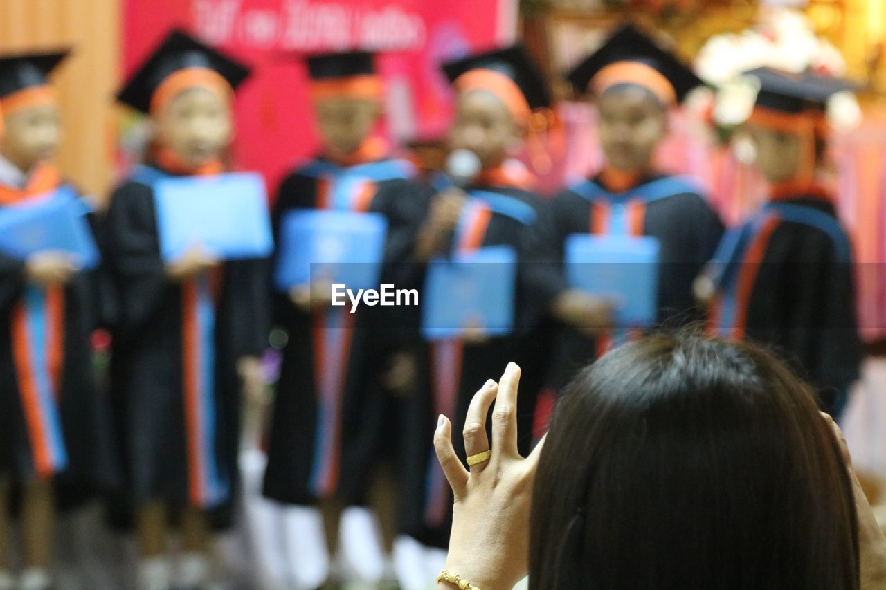 Rear view of woman against students wearing graduation gowns