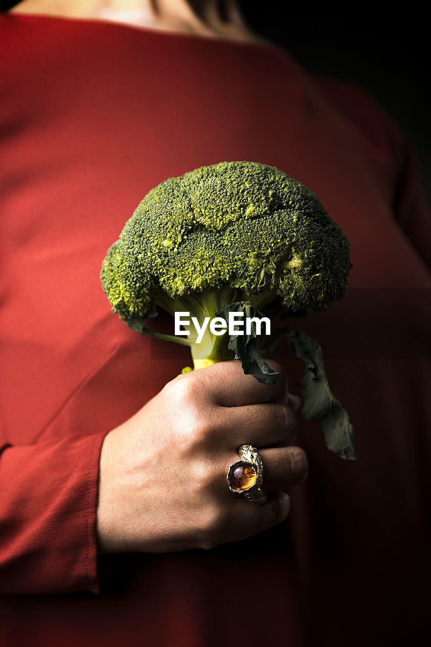 Woman in a tile-colored dress, and broccoli in hand