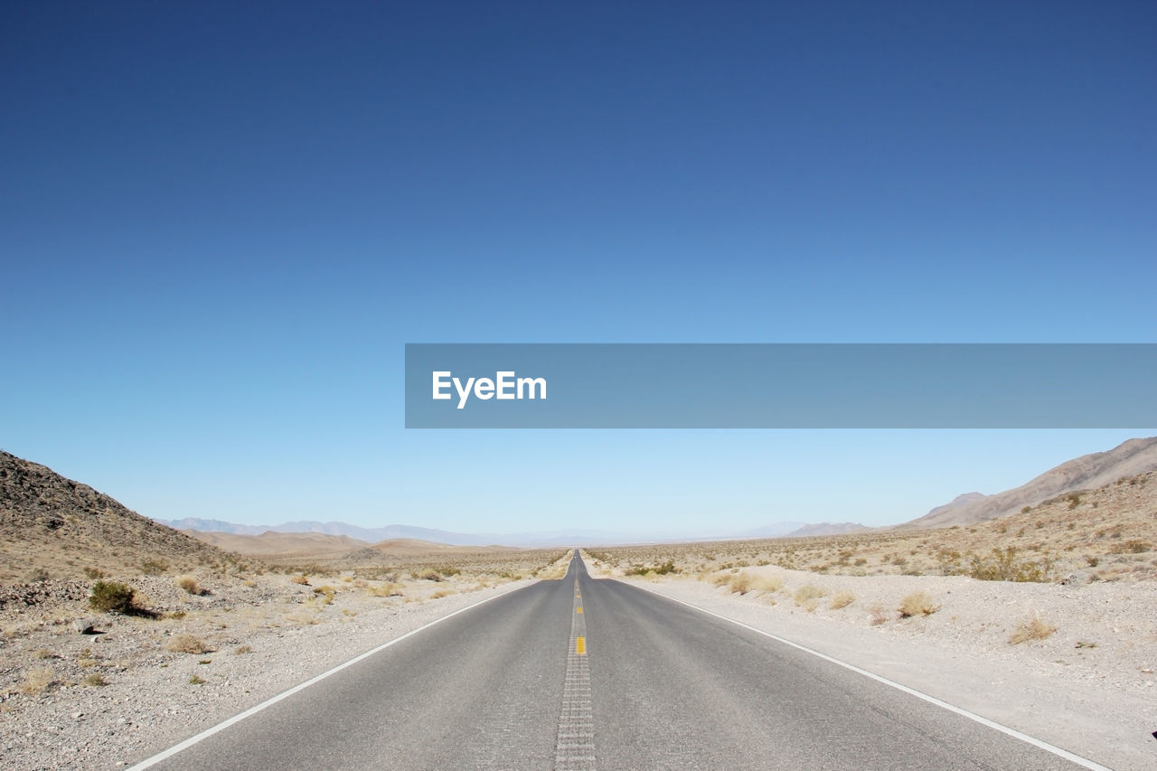 Empty road in desert against clear blue sky