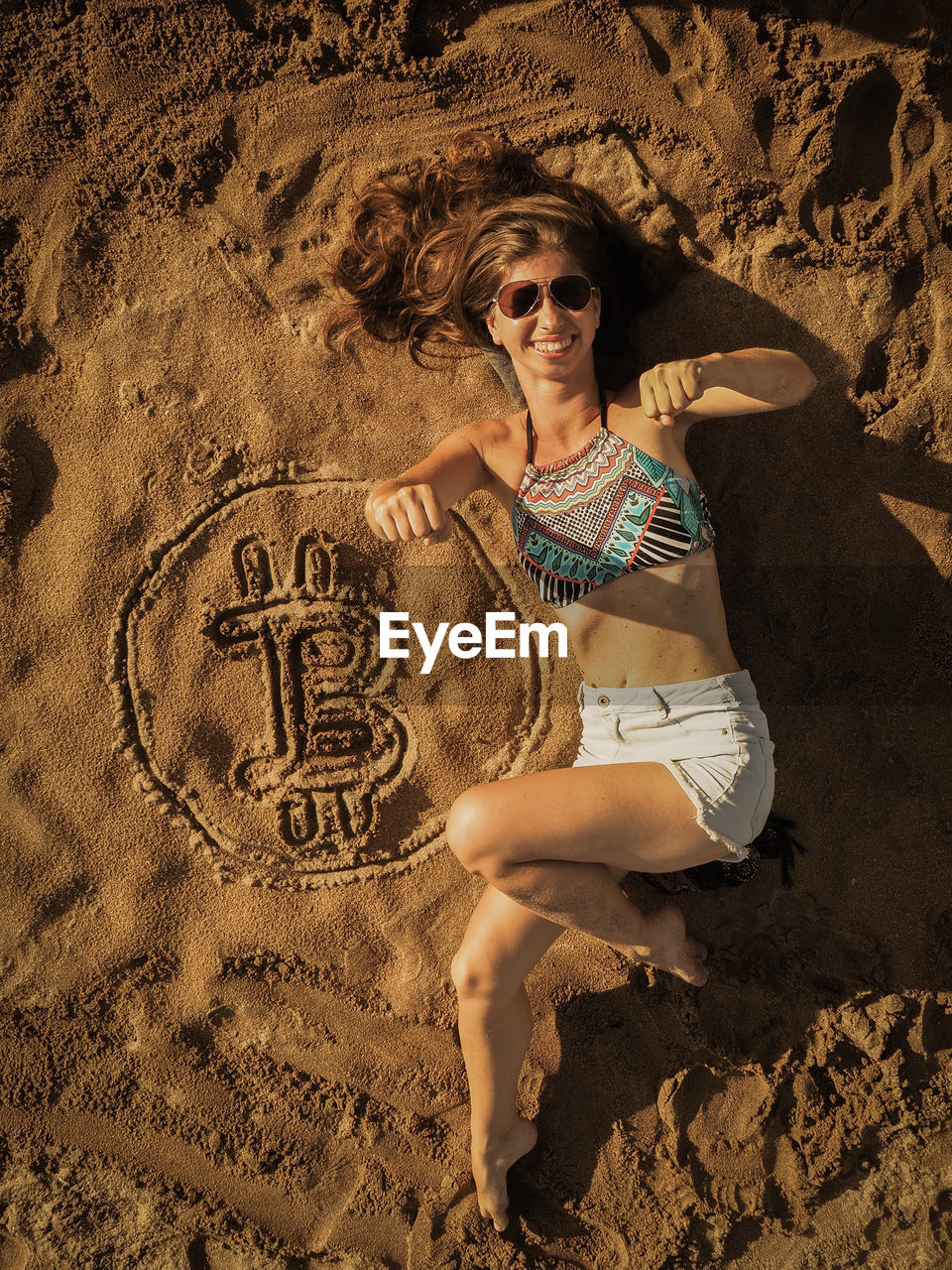 Full length of woman lying by bitcoin symbol at beach