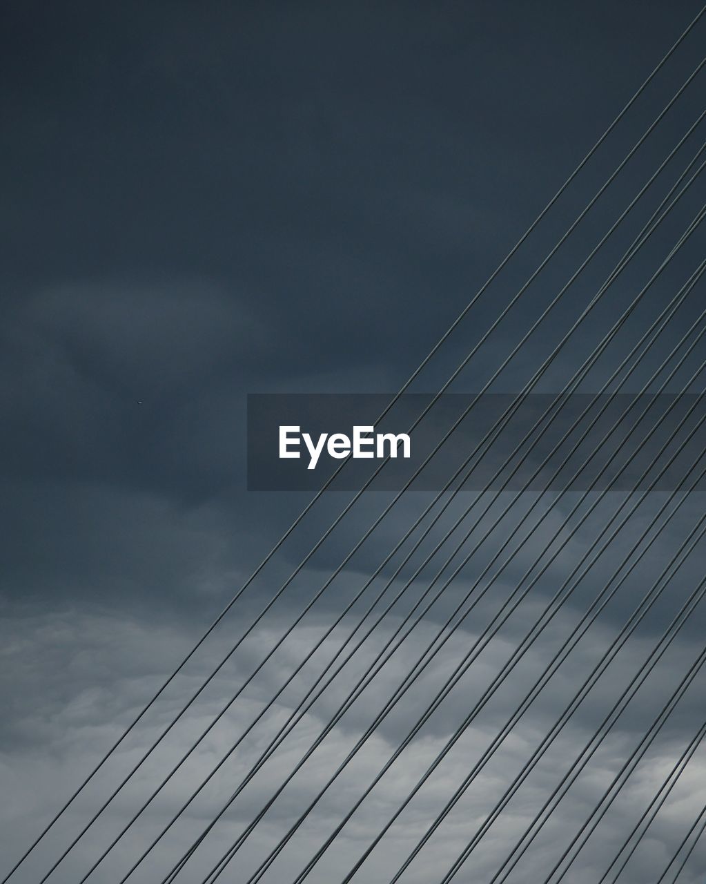 LOW ANGLE VIEW OF SUSPENSION BRIDGE CABLES AGAINST CLOUDY SKY