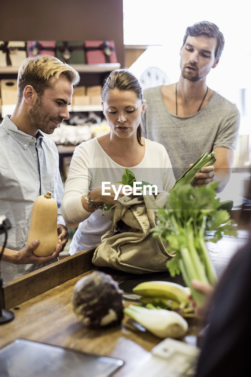 Friends discussing while shopping vegetables at supermarket checkout