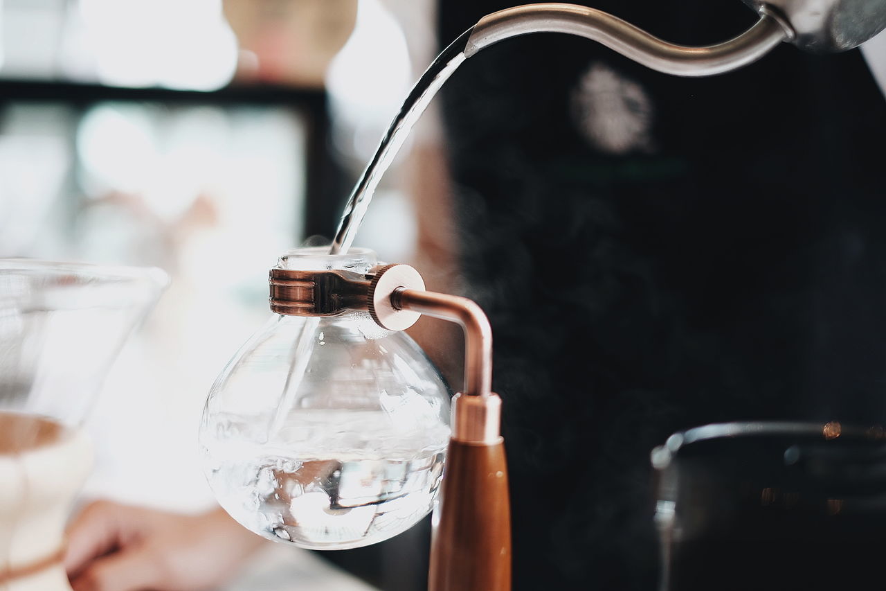 Midsection of person pouring water in container at cafe