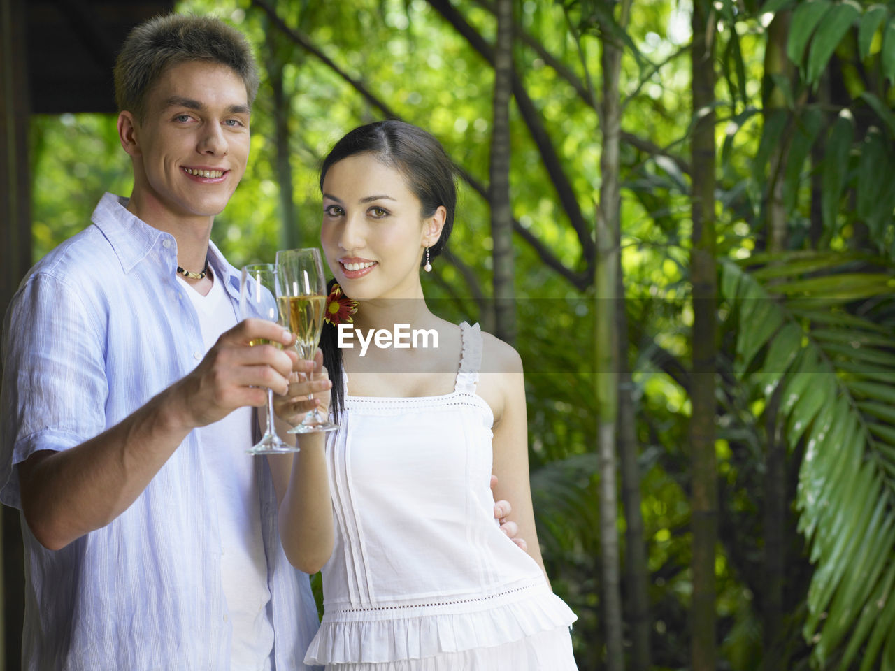 Portrait of smiling young couple with drink standing against plants