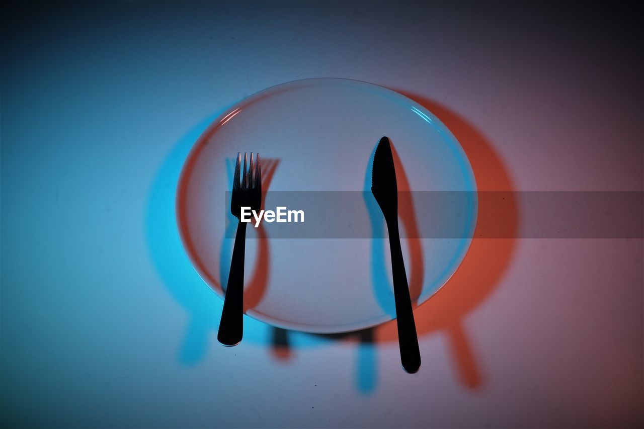 Directly above shot of white dish folk anf knife on plate against blue wall