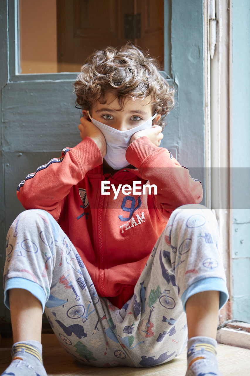 Portrait of boy wearing mask sitting against door