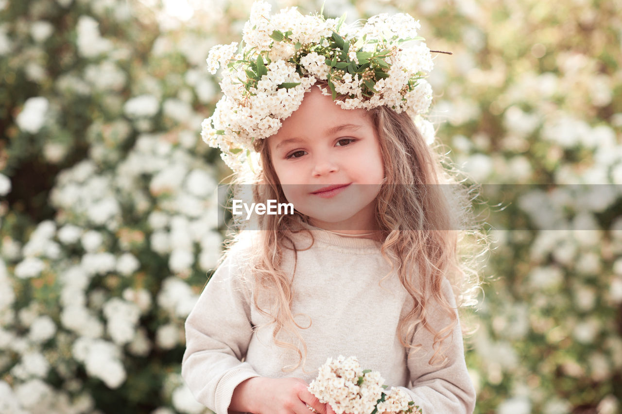 child, childhood, plant, flower, women, one person, portrait, flowering plant, bride, nature, innocence, dress, smiling, happiness, clothing, female, emotion, cute, toddler, wreath, spring, crown, front view, looking at camera, portrait photography, hairstyle, wedding dress, laurel wreath, royalty, celebration, long hair, fashion, flower arrangement, outdoors, blond hair, beauty in nature, person, day, looking, waist up, standing, bouquet, freshness, positive emotion, event, white, pink, tree, brown hair, fun, lifestyles, cheerful, fashion accessory, summer, focus on foreground