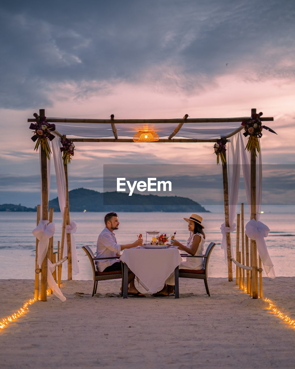 PEOPLE SITTING ON CHAIR AT BEACH DURING SUNSET