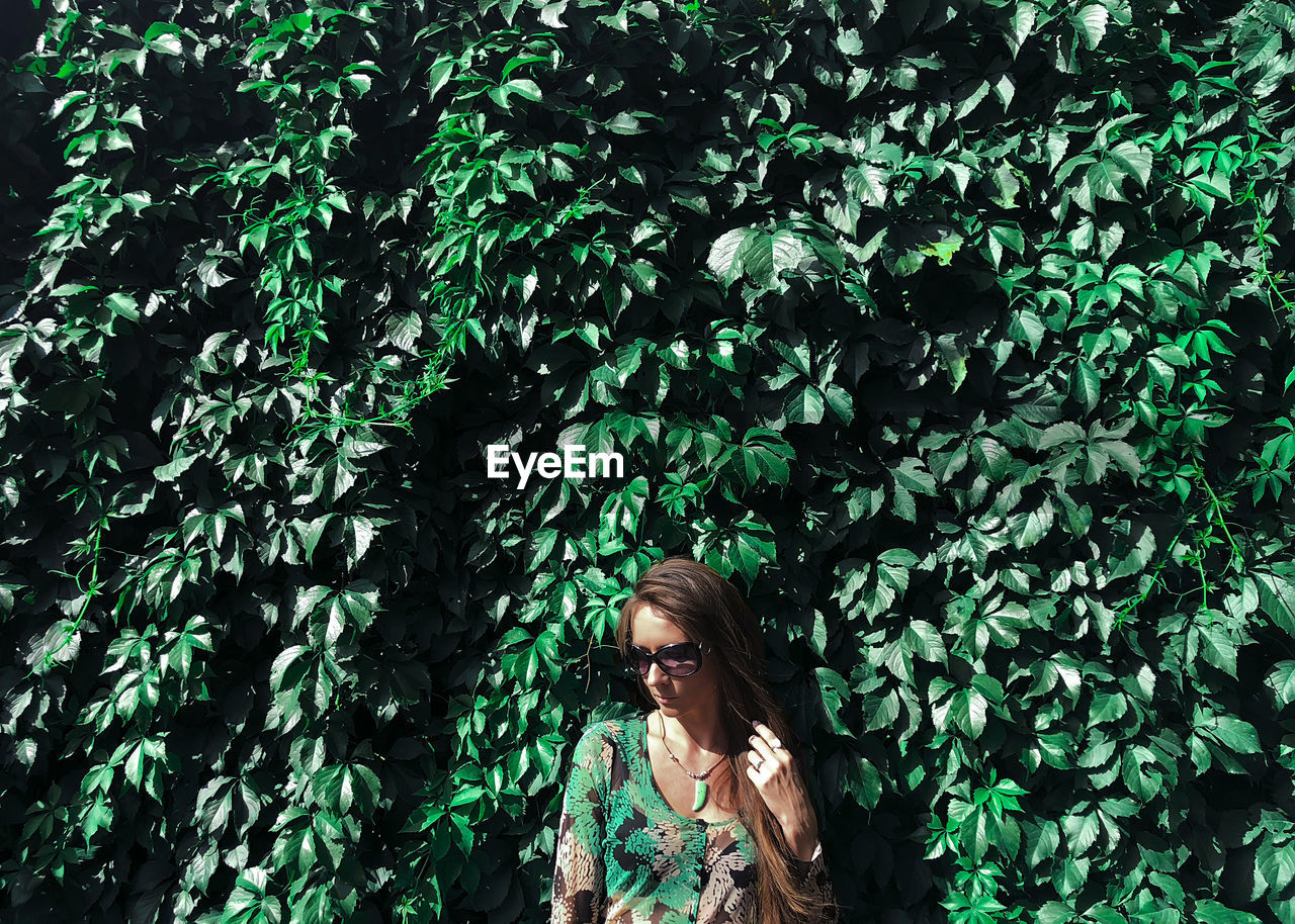 Woman wearing sunglasses looking away standing against plants