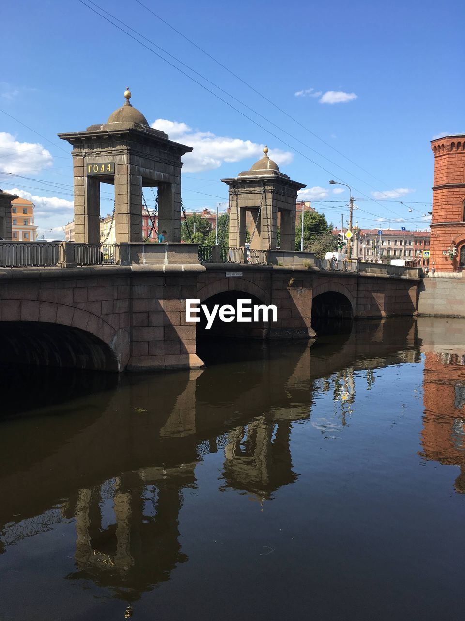 Arch bridge over river by buildings against sky