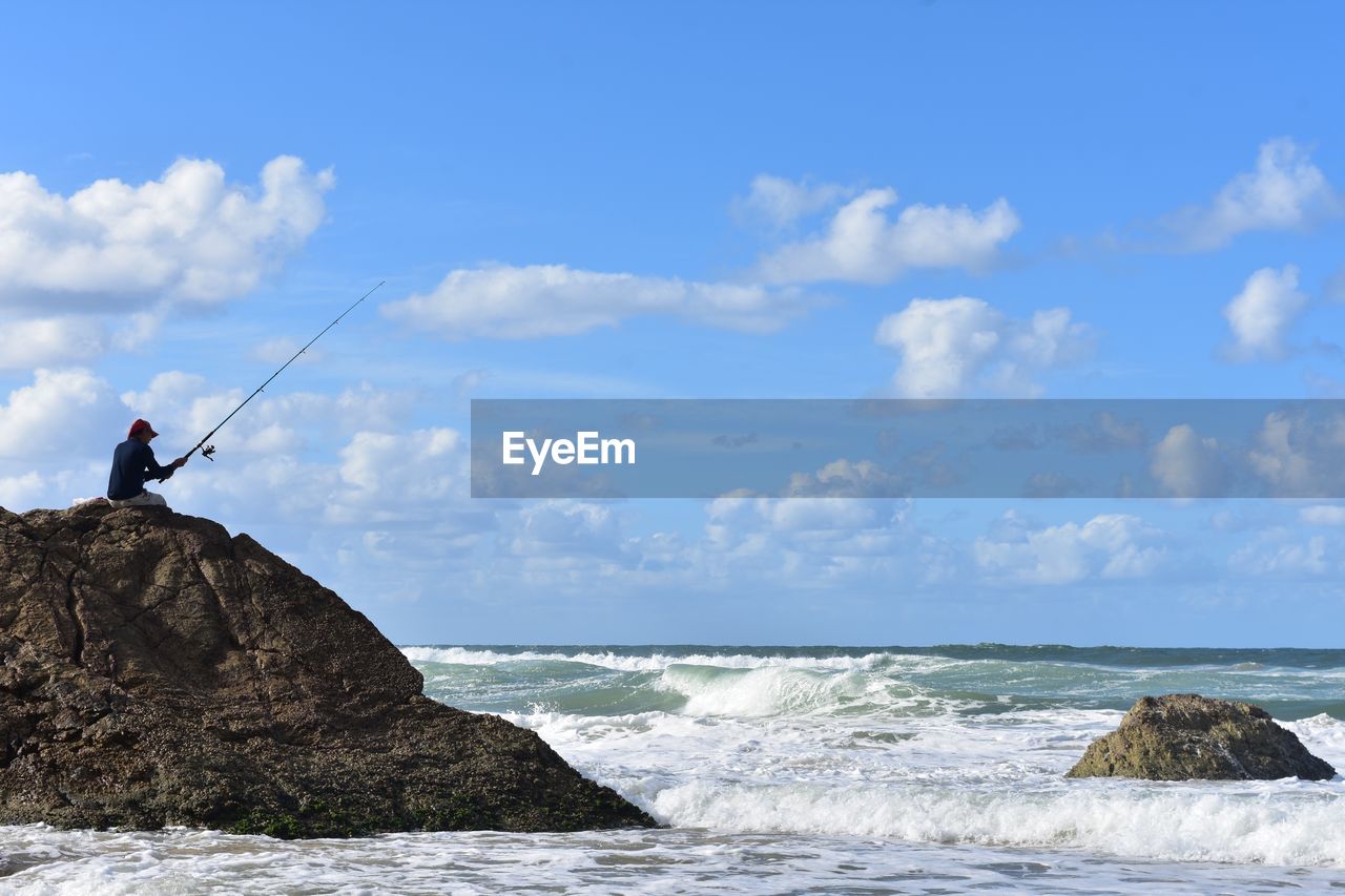 MAN STANDING ON ROCK AGAINST SEA