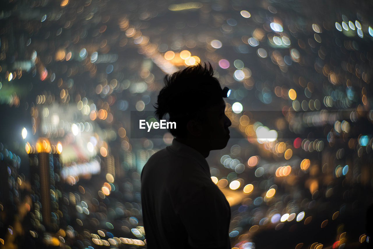 Side view of man standing against defocused lights