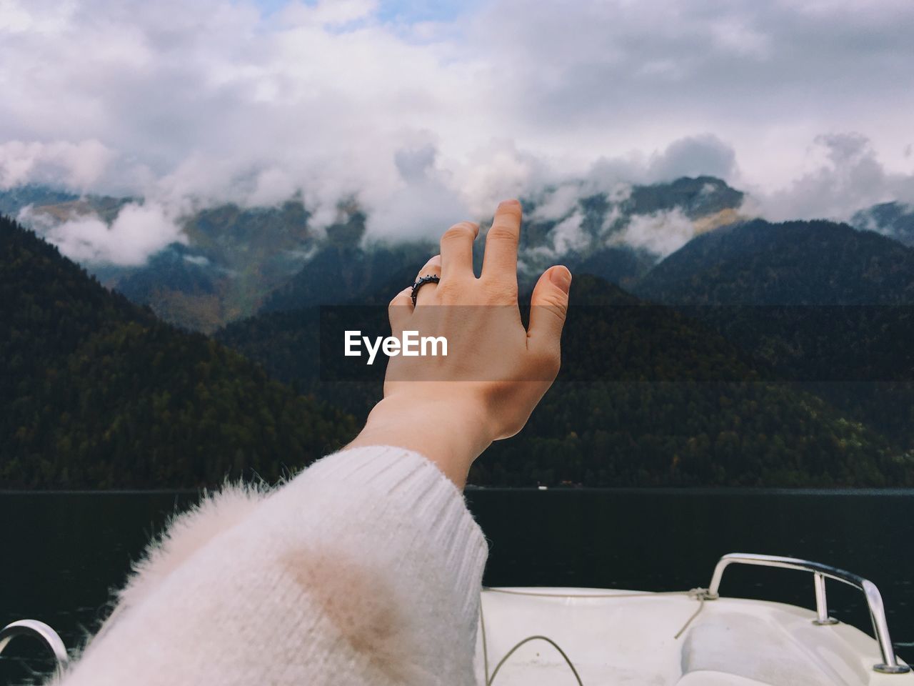 Cropped hand of woman against mountain range against sky