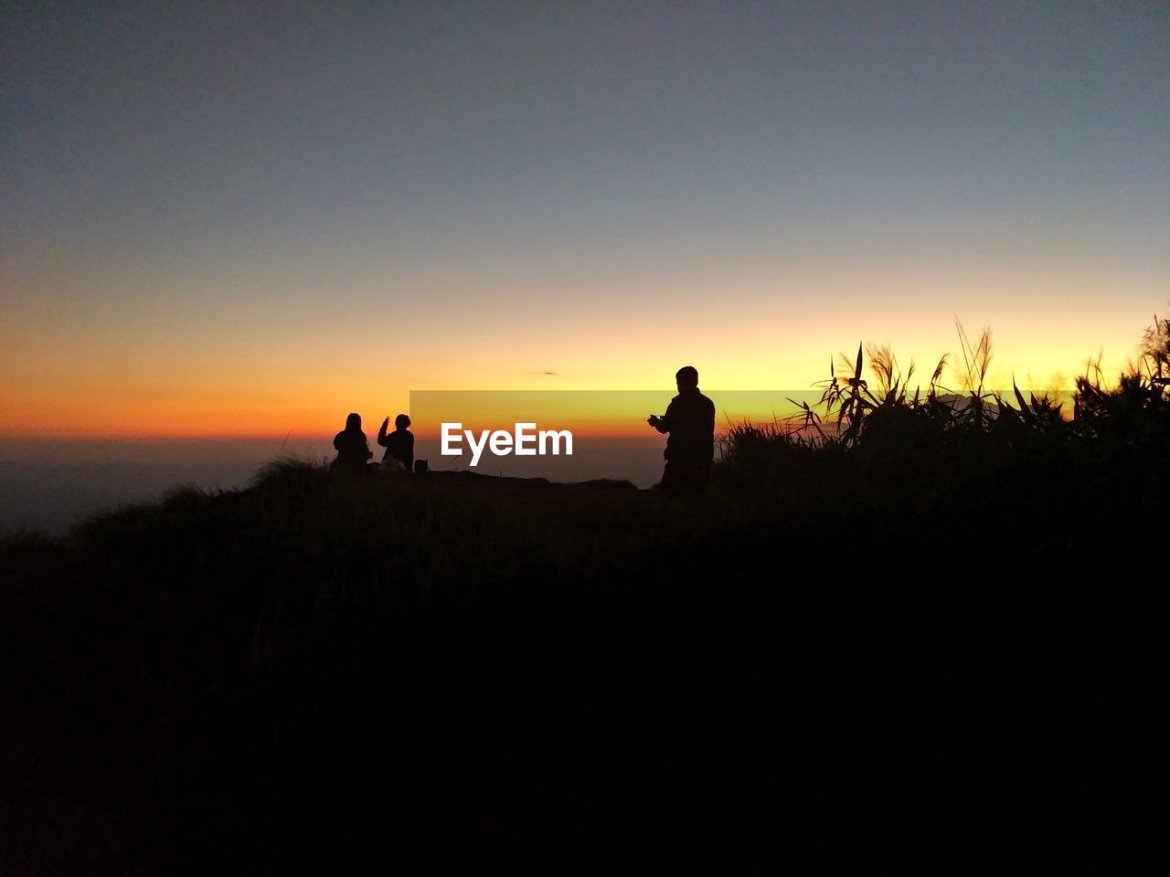 SILHOUETTE PEOPLE ON LAND AGAINST ORANGE SKY