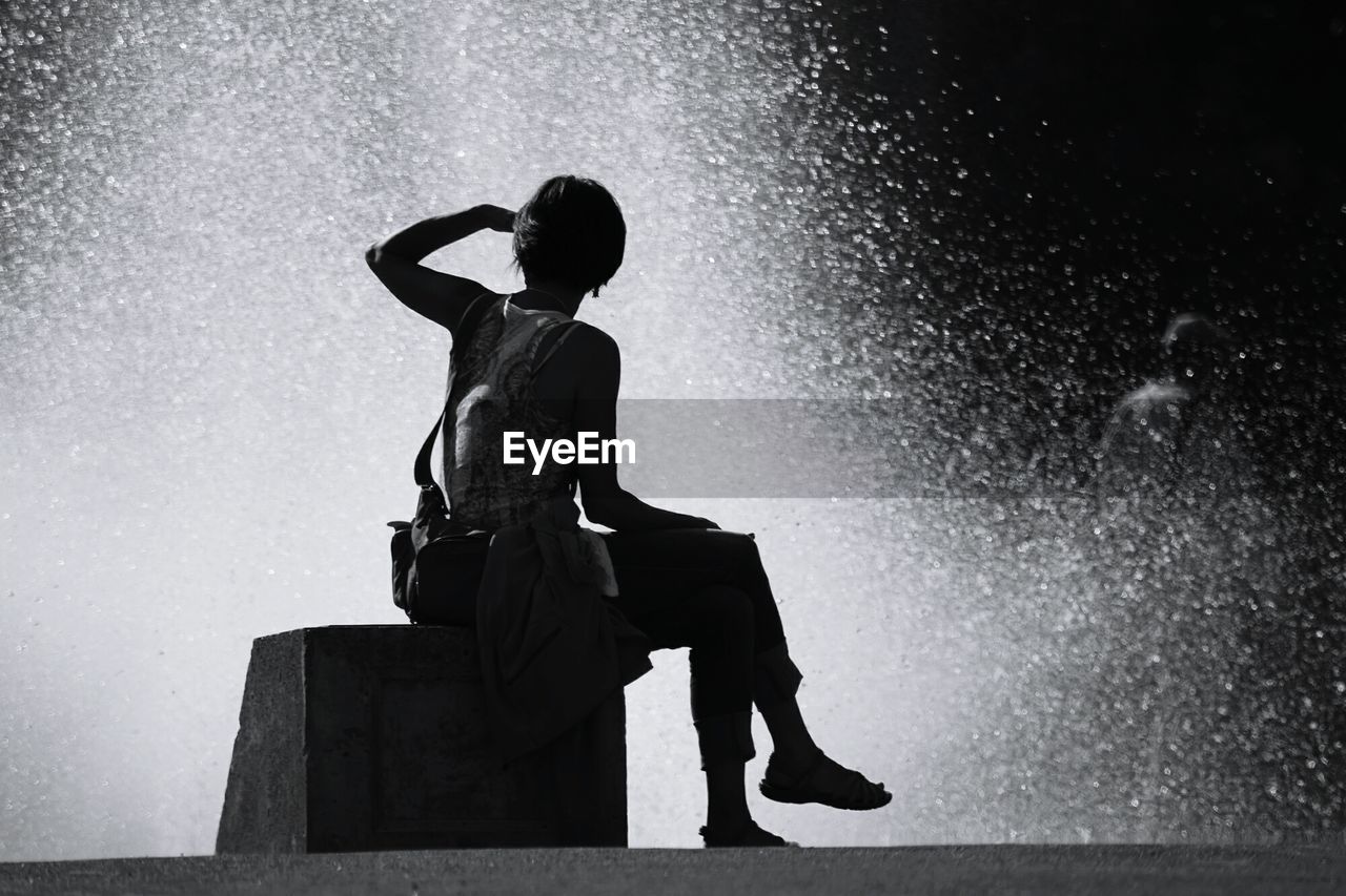 Rear view of woman sitting by fountain