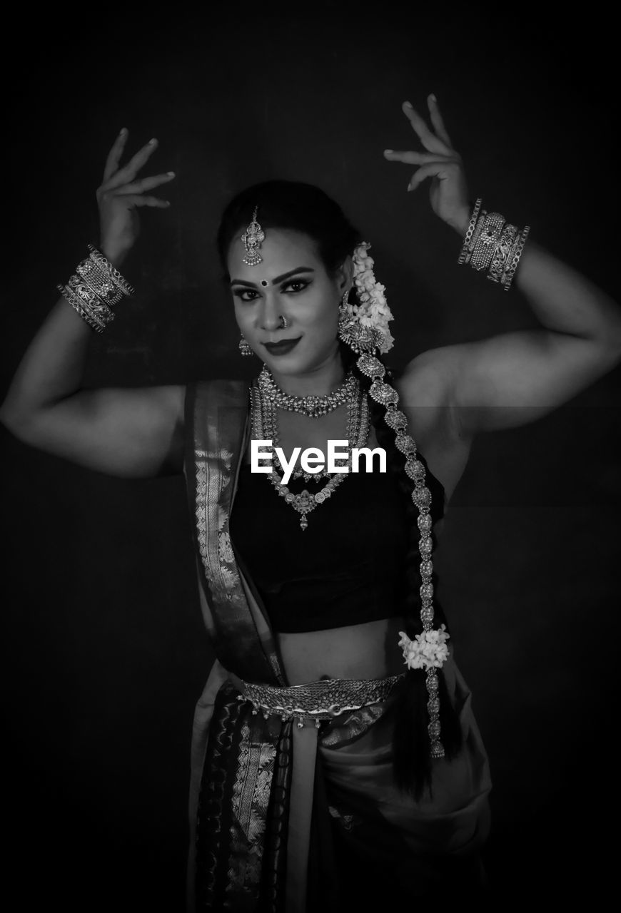 Portrait of young woman standing against black background