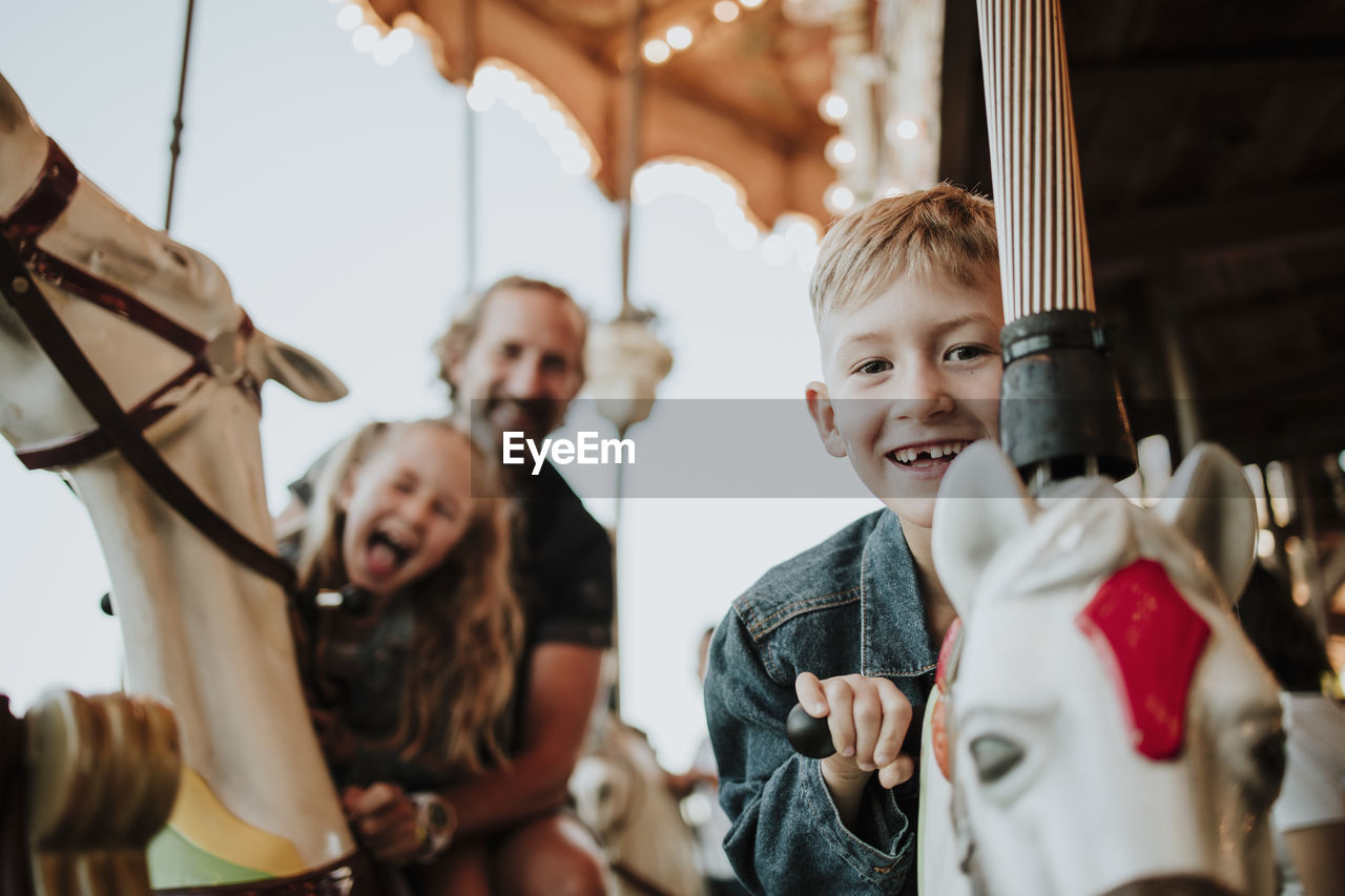 Smiling boy enjoying carousel ride with family at amusement park