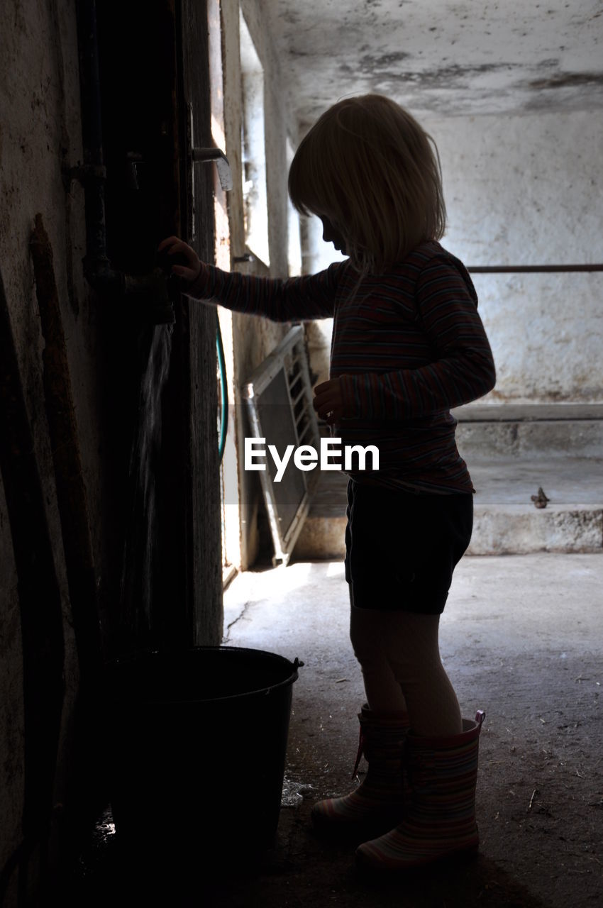 Child filling bucket of water in shed