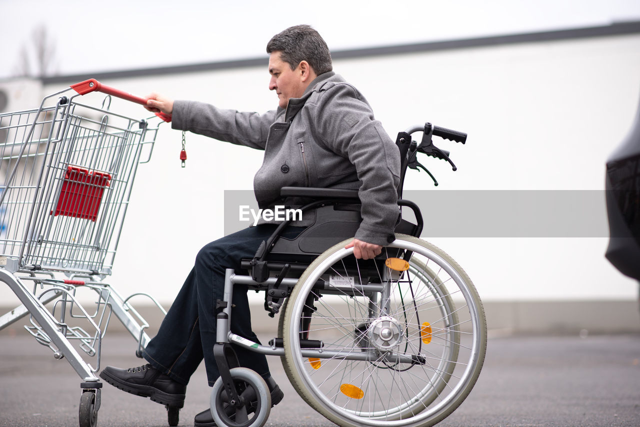 Physical disabled person in a wheelchair pushing shopping cart