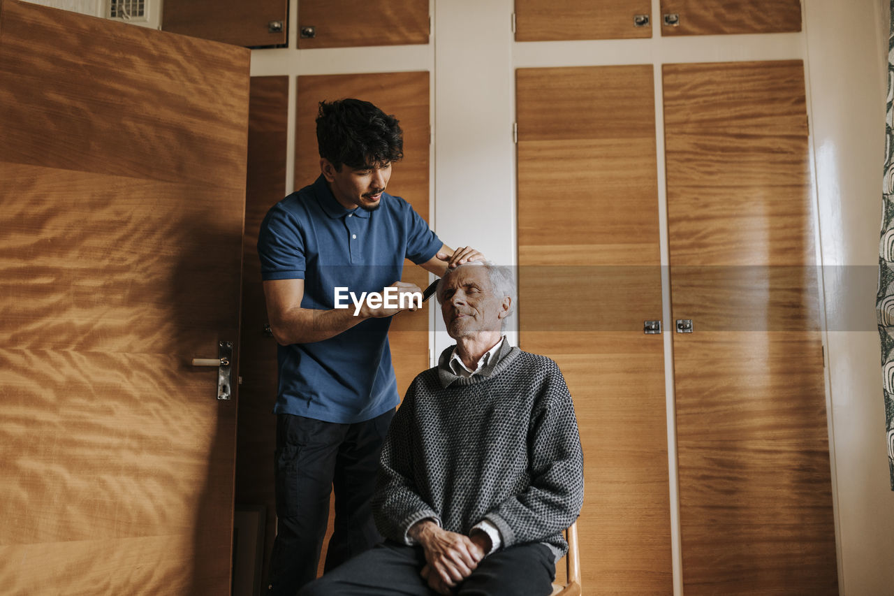 Male healthcare worker taking care of senior man sitting at home