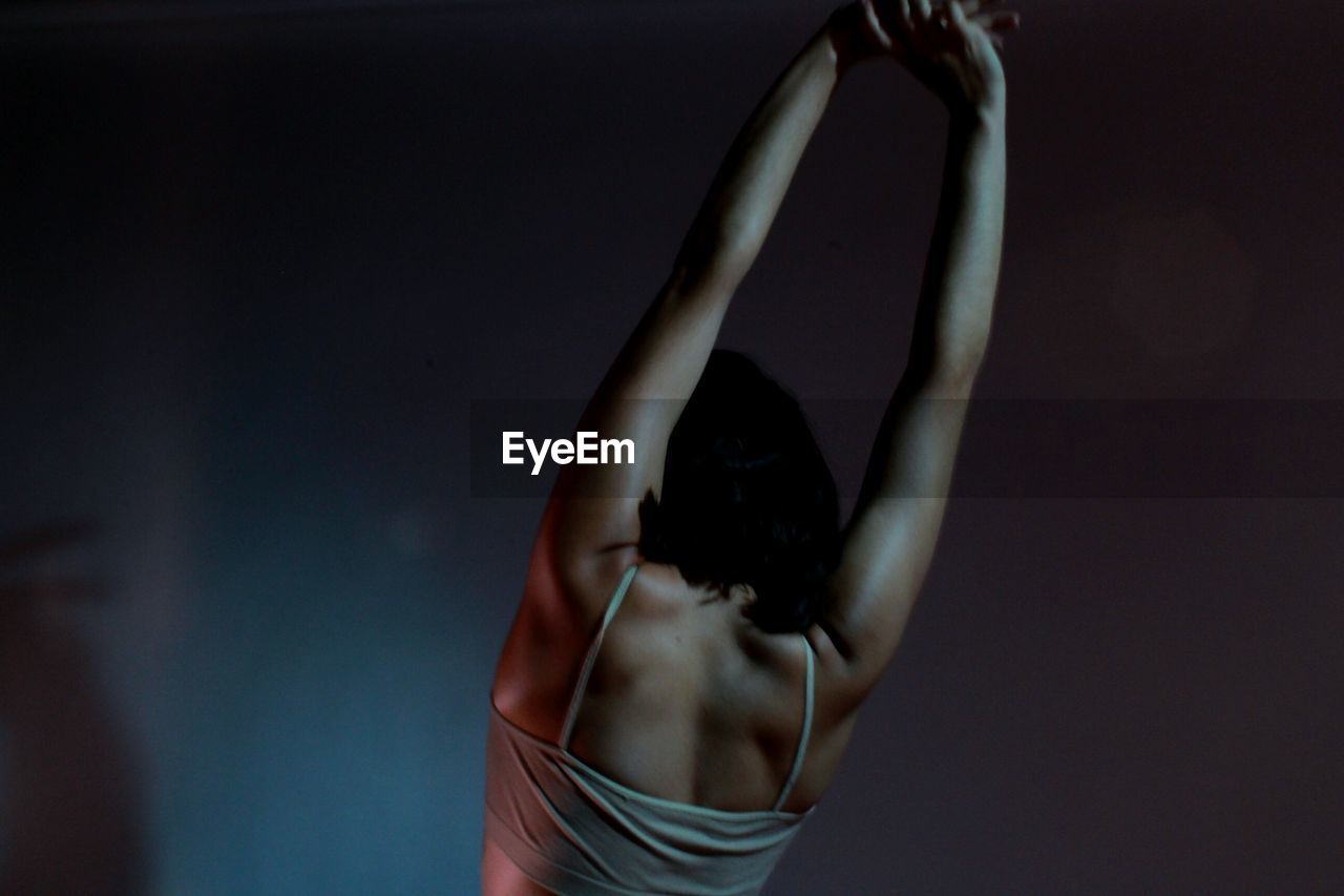 Rear view of woman with arms raised against wall