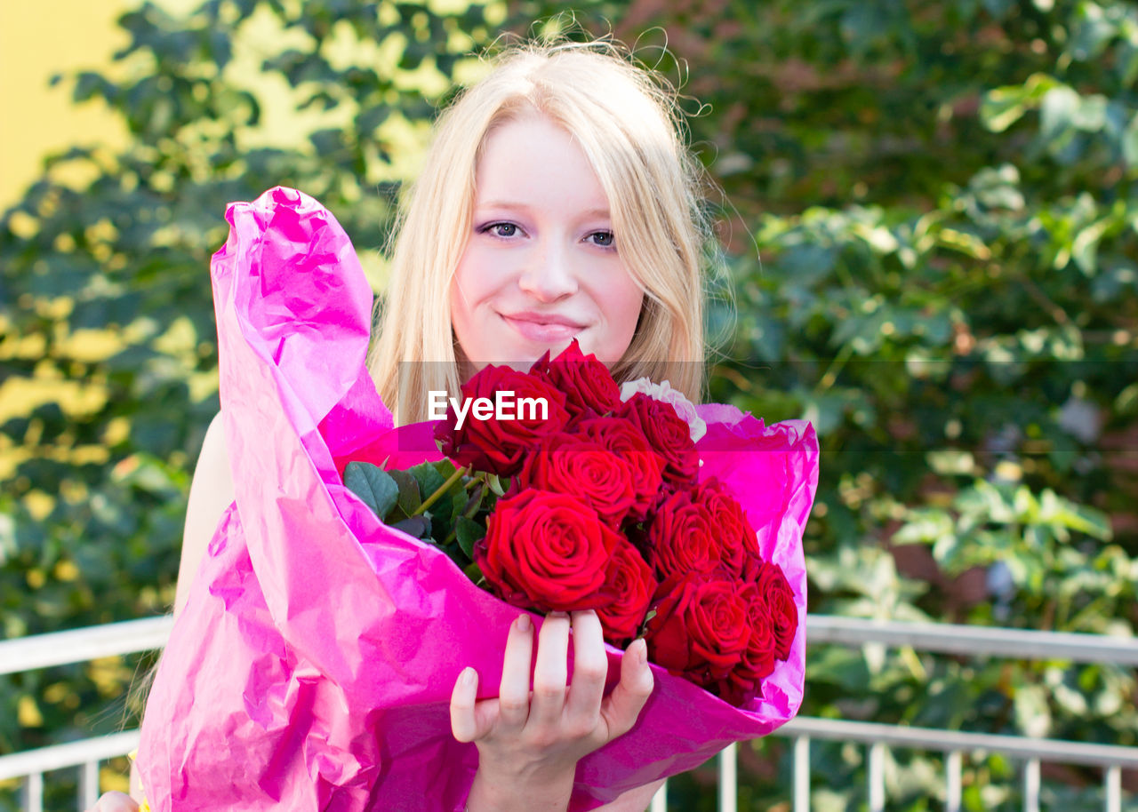 Portrait of smiling young woman holding rose bouquet