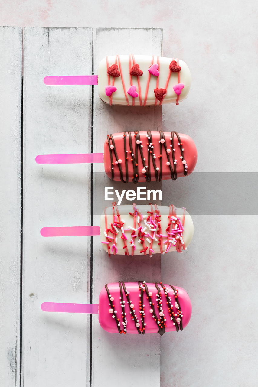 Vertical view of valentine cakesicles on a white rustic wooden board.
