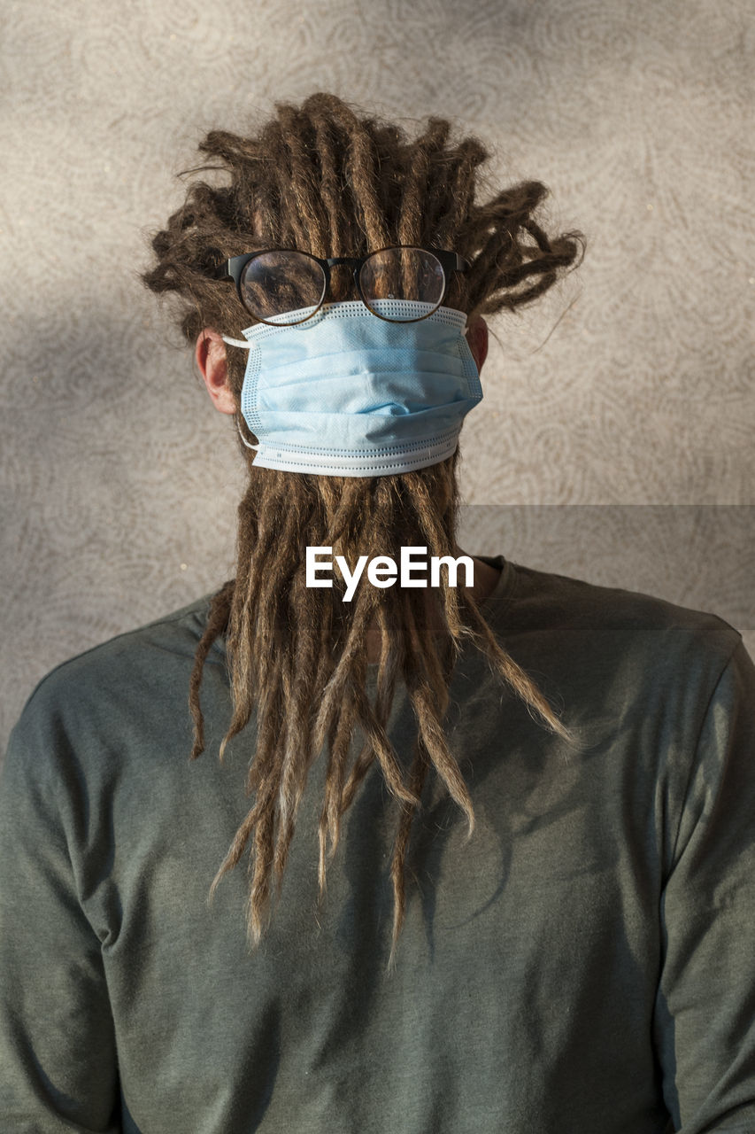 Woman wearing mask with dreadlocks against wall