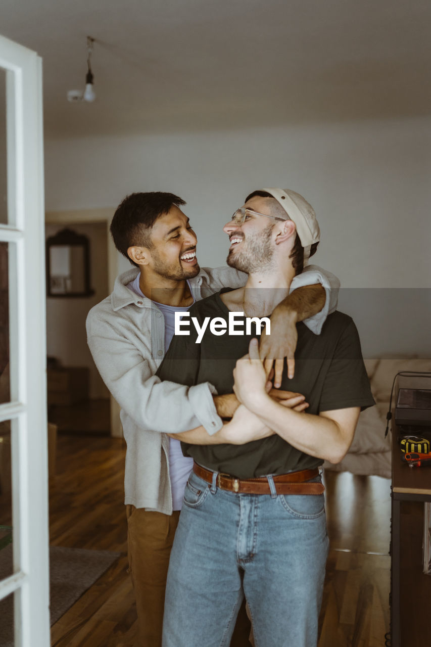 Happy gay couple looking at each other standing in bedroom at home