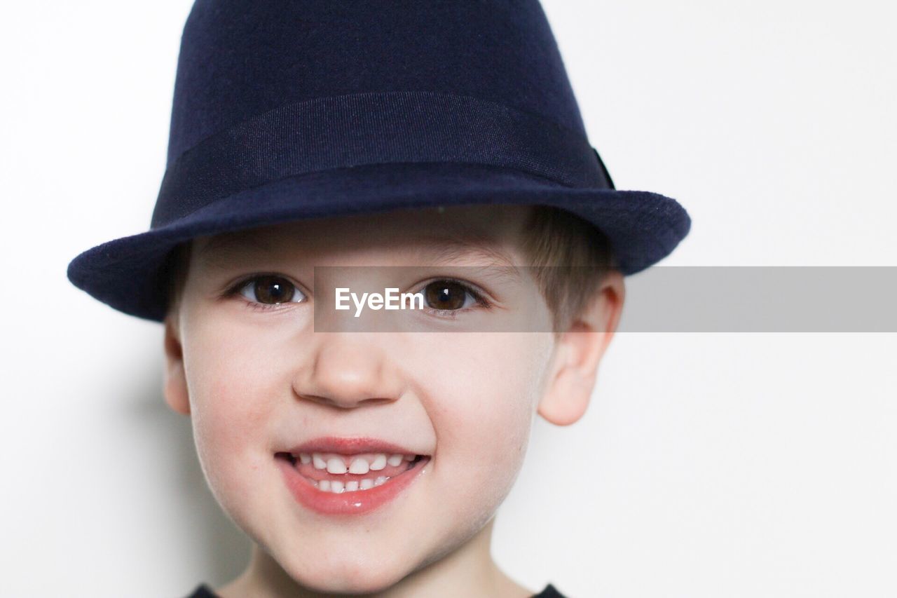 Close-up portrait of smiling boy wearing hat against white wall