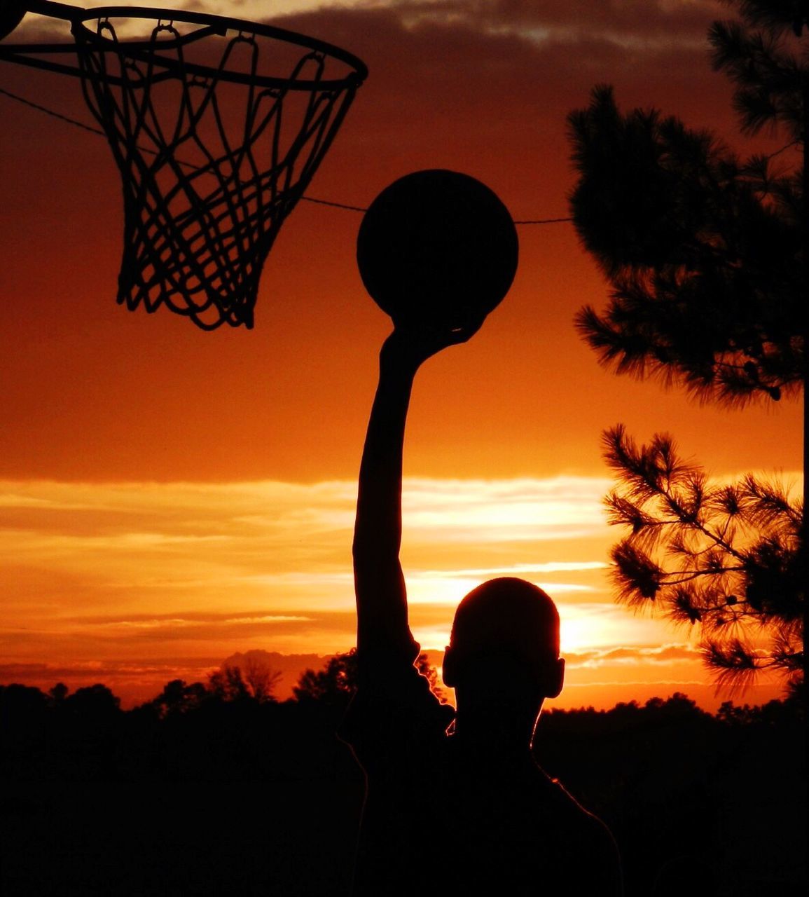 Silhouette man holding basket ball against cloudy sky during sunset