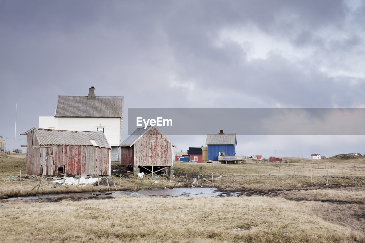 Old houses on field against cloudy sky