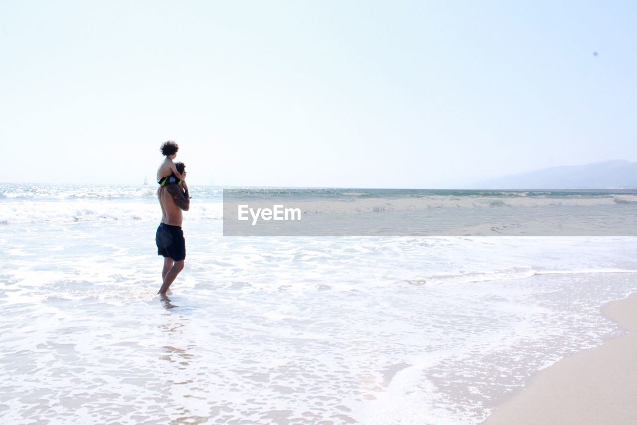 Father and son walking on wave at beach