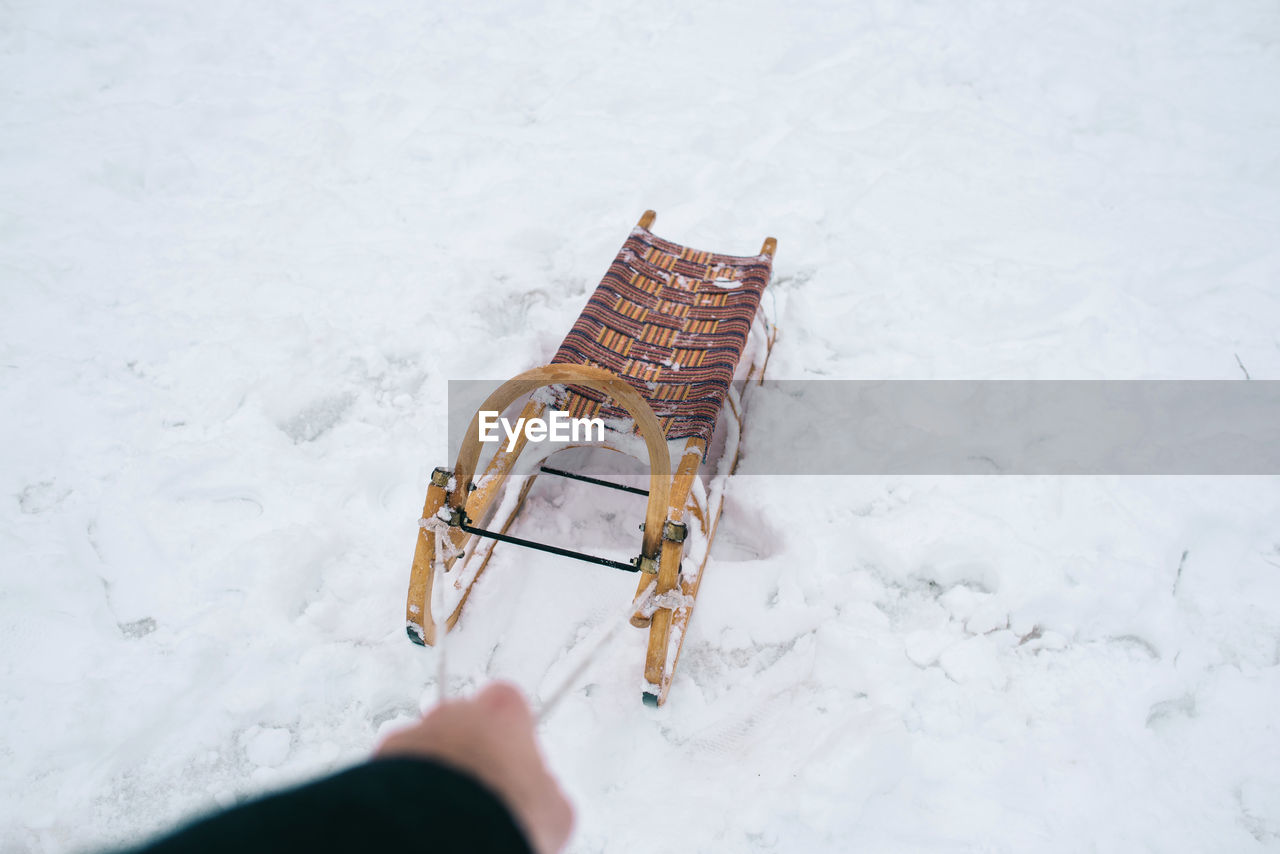 Cropped hand of person pulling sled on snow