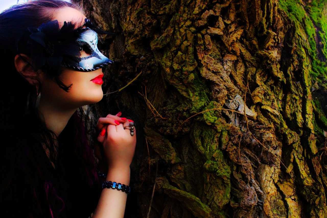 Close-up of woman wearing venetian mask while leaning on tree