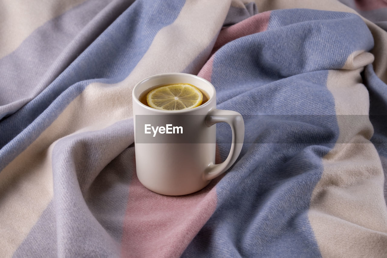 Autumn composition of soft warm scarf in pastel colors and ceramic mug with hot tea