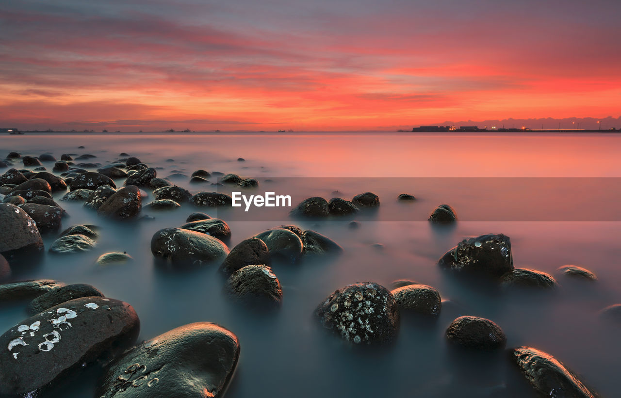 Scenic view of rocks in sea against sky at sunset