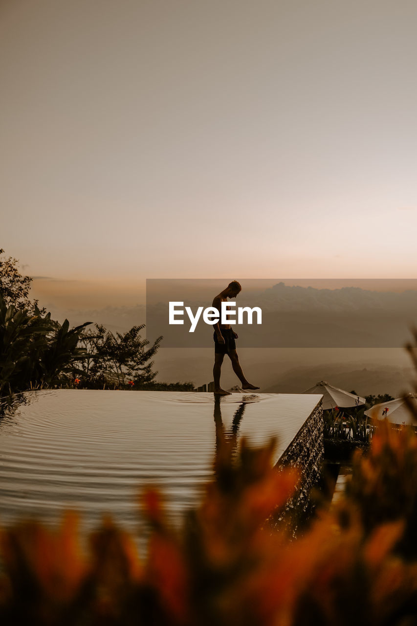 Rear view of woman walking on beach against sky during sunset