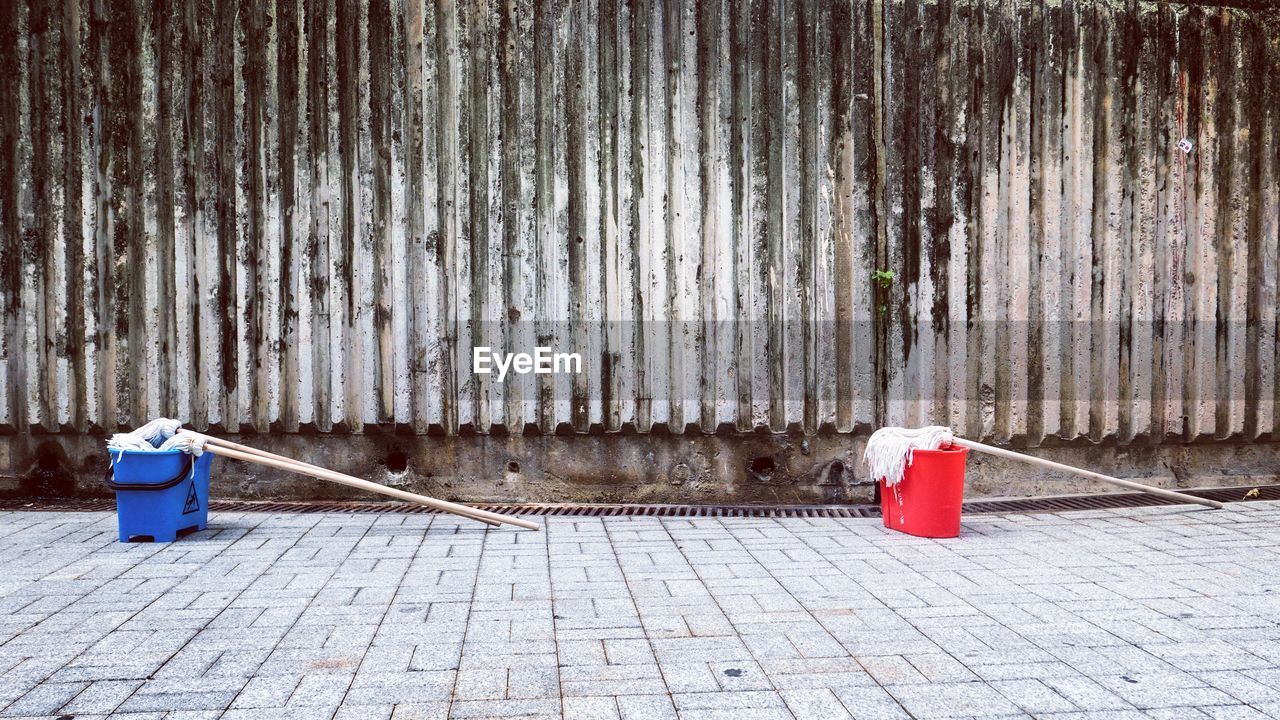 Mops in red and blue buckets on footpath by old wall