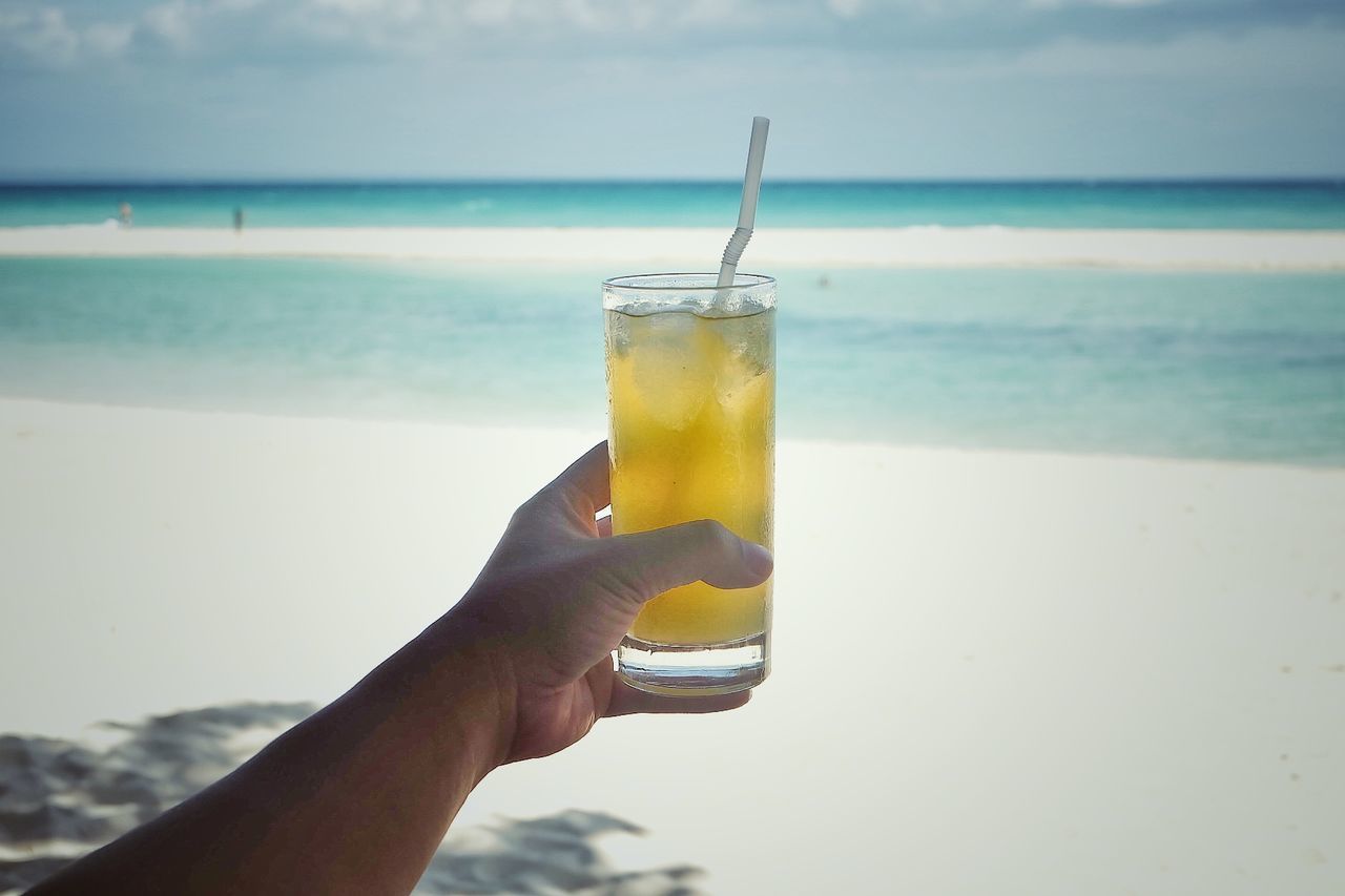 Close-up of hand holding drink at beach against sky