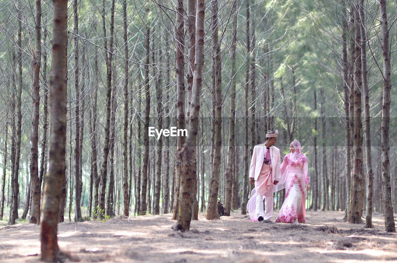 Bride and groom walking amidst trees in forest