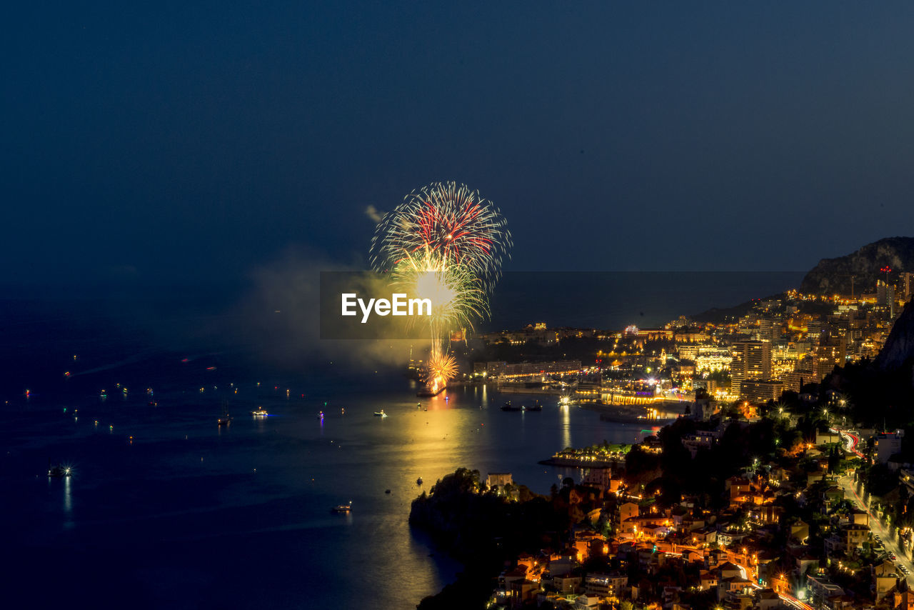 Firework display over illuminated city against sky at night