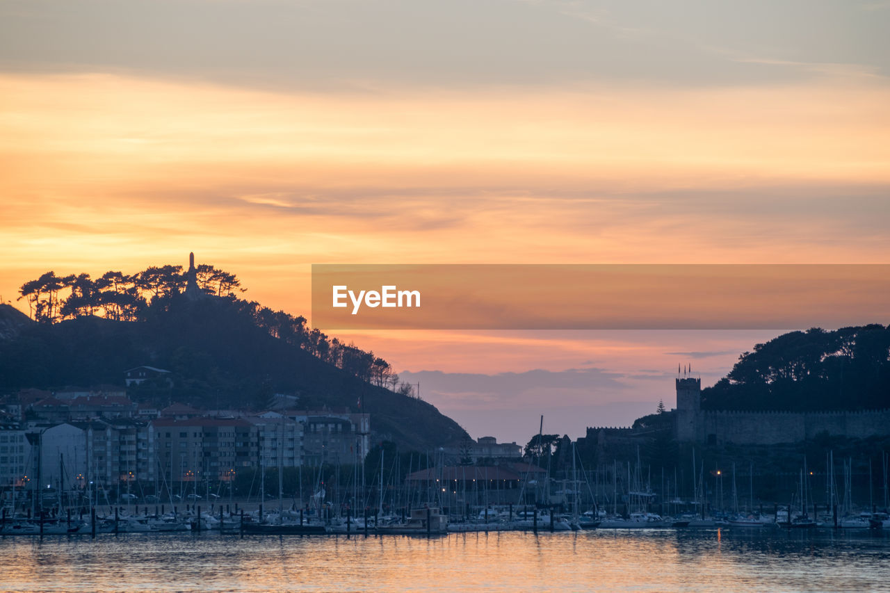 Scenic view of townscape by river against sky during sunset