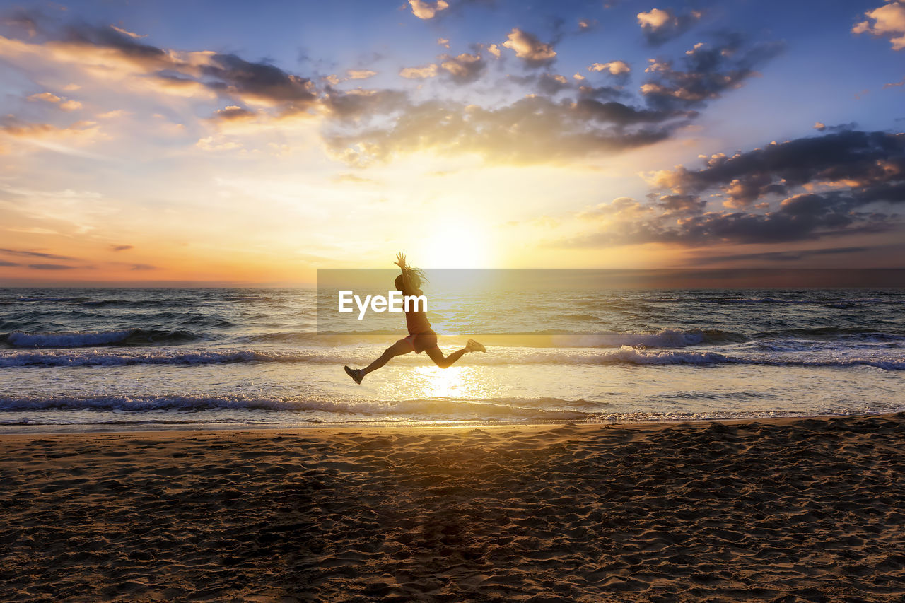 Full length of woman jumping beach during sunset