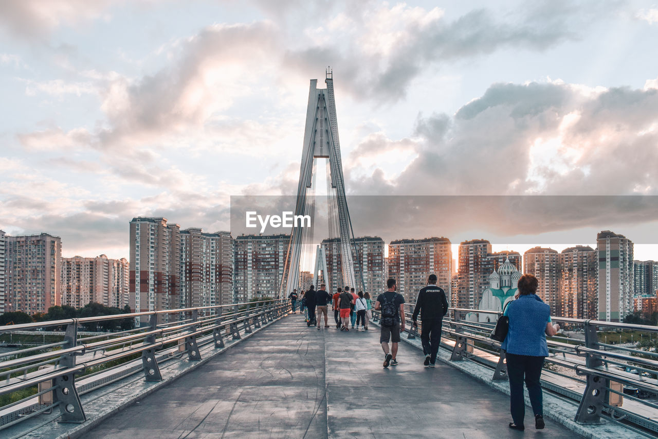 People walking on bridge against cloudy sky